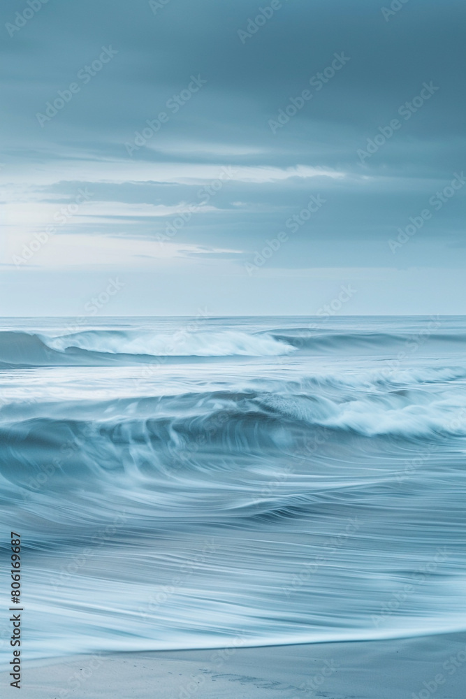 Fototapeta premium A tranquil and serene scene of sky blue and soft gray waves, merging gently in a calming dance that evokes the peacefulness of an overcast day at the beach.