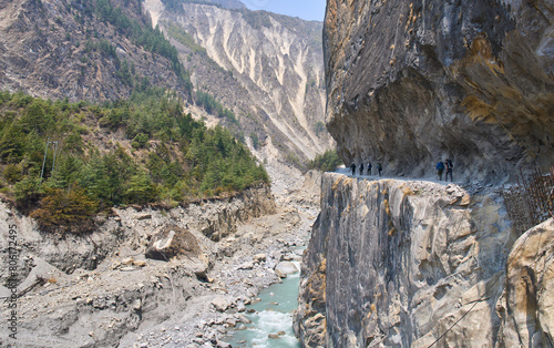 Tourists on the Annapurna circuit trek near the village Chame in the Annapurna Conservation Area. A hiking path above the Marshyangdi River. Turquoise color of the river.