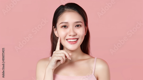 Beautiful young Asian woman pointing finger to her cheeks on isolated pink background. Facial and skin care concept for commercial advertising.