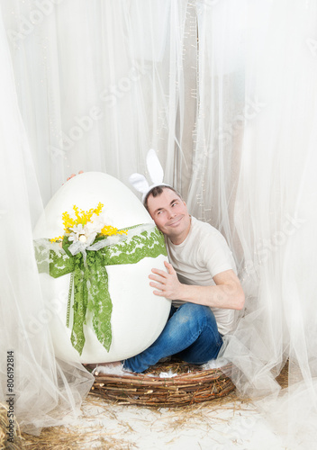 Funny man with rabbit ears sitting in the nest Easter holiday concept and holding egg