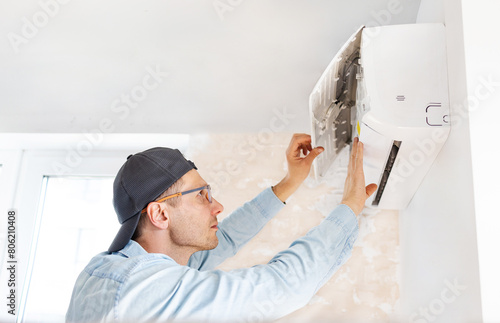 Young male technician repairing air conditioner indoors.