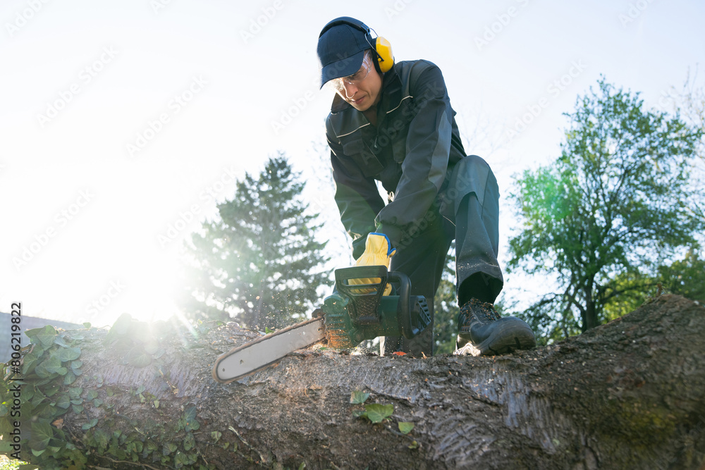 A man in uniform cuts an old tree in the yard with an electric saw. A man in uniform cuts an old tree in the yard with an electric saw.