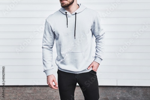 Man in a white hoodie poses for a mock-up design. A fashion template for print and branding. An outdoor portrait of a young man in a casual hooded pullover. mock-up template of a white hoodie. No face