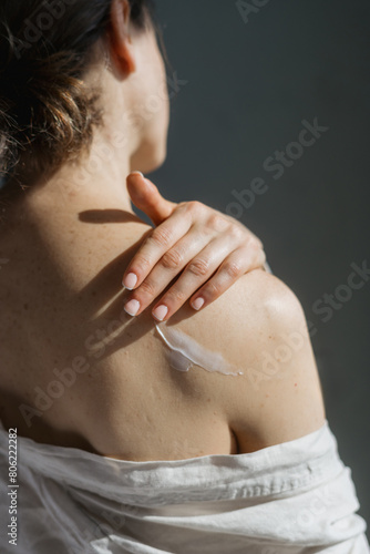 Woman applying soft cream on shoulder, vertical shot