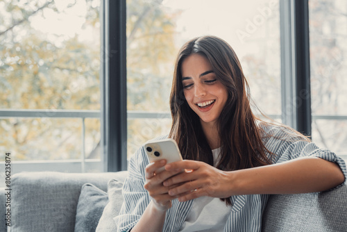 Fotografía Happy pleasant millennial woman relaxing on comfortable couch, holding smartphone in hands
