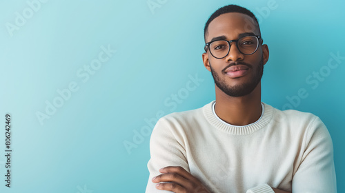 Stylish young man wearing glasses and a white sweater, posing confidently against a soft blue background, exuding a calm and modern vibe. photo
