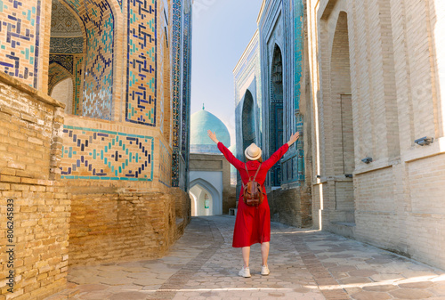 tourist woman in red dress clothes stands in the Shah-i-Zinda Ensemble in Samarkand, Uzbekistan