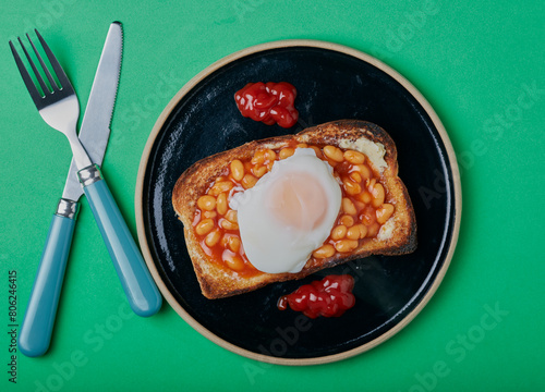 Beans on toast with a poached egg on top with tomato sauce,on a green background. © Mark