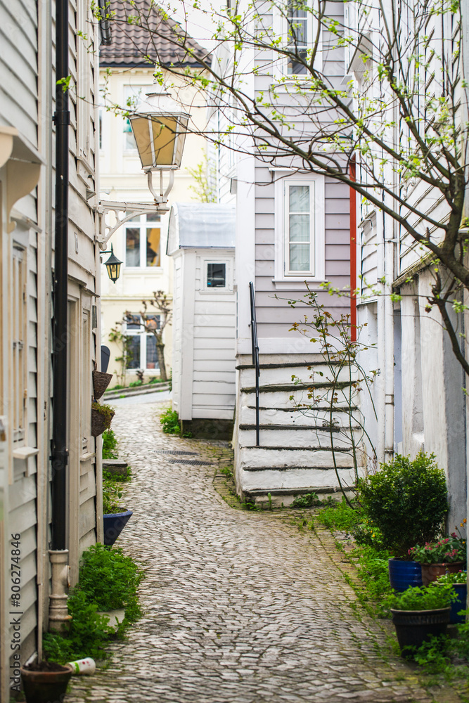 Narrow cobblestone street lined with traditional white wooden houses in the old town in spring. Bergen, Norway Heritage, sightseeing. Narrow cobblestone street lined with traditional white wooden houses in the old town in spring. Bergen, Norway Heritage, sightseeing.
