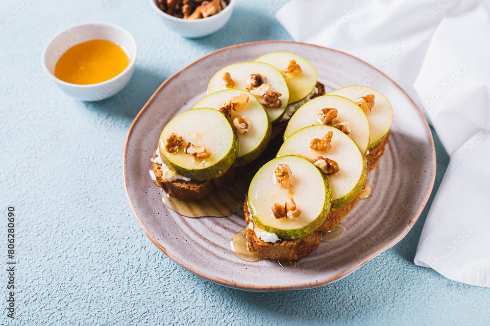 Pieces of pear, ricotta, honey and nuts on rye bruschettas on a plate on the table