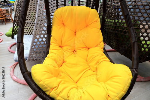 Rattan cocoon chair, garden furniture with yellow cushion in store. Beautiful fashionable modern wicker furniture, sofa, rocking chair cocoon for interior