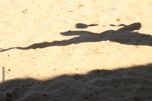 Woman holding a racquet with the shadow projected in the sand. 