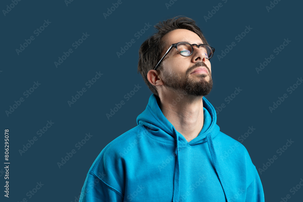 Obraz premium A man wearing glasses is looking upwards towards the sky, his expression curious and thoughtful. He is standing over blue background