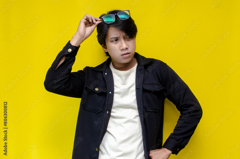 Fototapeta premium man feeling uncertain and unsure. Thoughtful asian man thinking and wondering with hand touching skin as thinking gesture isolated over yellow background.
