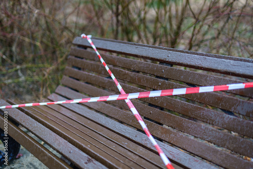 A park bench cordoned off with red and white striped barrier tape