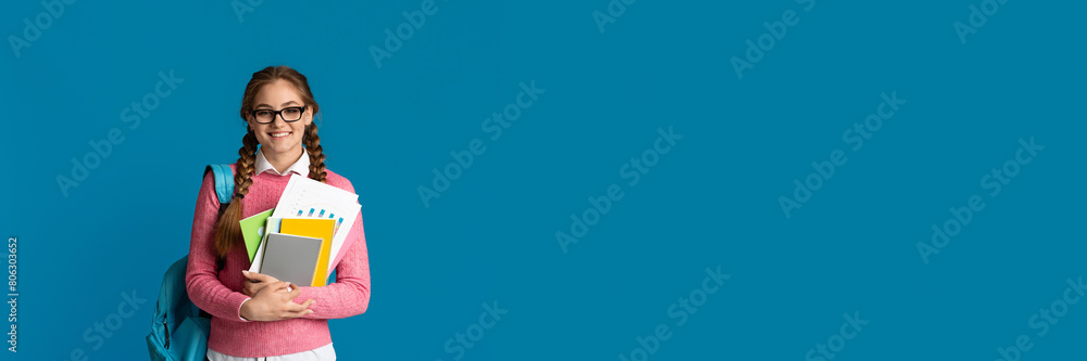 Modern student concept. Cute smiling girl teenager with notebooks and backpack posing on blue studio background, copy space Modern student concept. Cute smiling girl teenager with notebooks and backpack posing on blue studio background, copy space