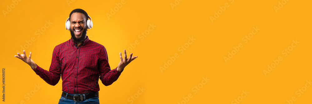 Fototapeta premium Online Music. Excited african american guy wearing white headset and dancing with joy isolated on yellow studio wall, copy space