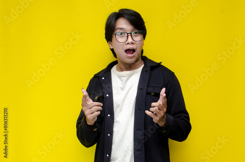 wow expression of asian man with glasses pointing finger to copy space showing something good. 