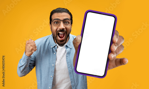 Indian man is holding up a cell phone in his hand, and his face displays a surprised expression. It seems that he has received unexpected news or seen something shocking on the screen.