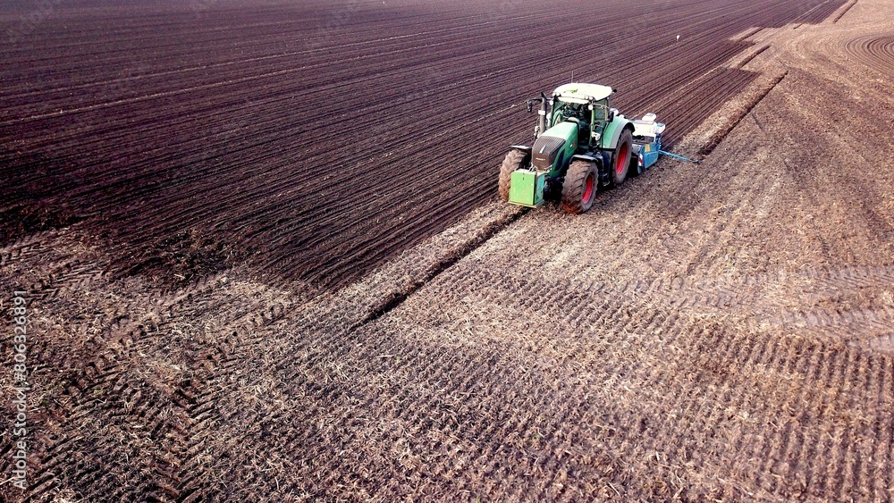 Obraz premium Traktor mit Sämaschine wirbelt bei der Aussaat von Mais Staub auf einem Acker auf, Landwirtschaft, Drillsaat, Pflanzenanbau, Luftbild