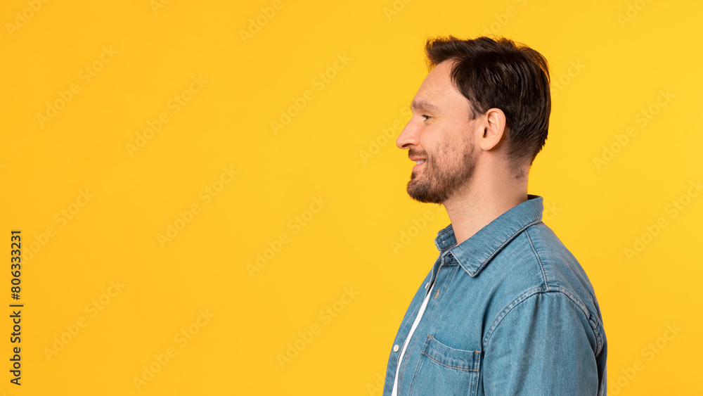 A man is standing in front of a bright yellow background. He is facing forward with a neutral expression. The background color contrasts sharply with his dark-colored clothing, copy space A man is standing in front of a bright yellow background. He is facing forward with a neutral expression. The background color contrasts sharply with his dark-colored clothing, copy space