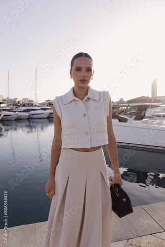 beautiful woman with dark hair in elegant classic clothes with accessories posing at the marina with the yachts in Cyprus
