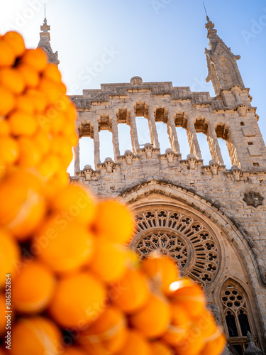 Fira de la Taronja orange festival in Sóller's Plaça de la Constitució square, featuring a portrait of the fountain adorned with a defocused heap of ripe oranges, with Sant Bartomeu church in backdrop