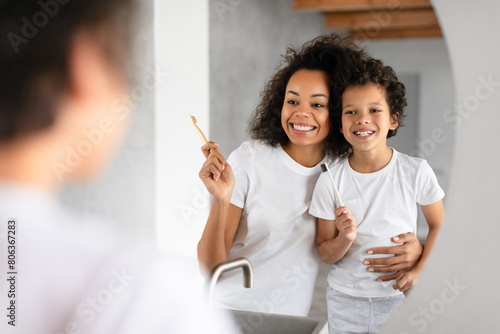 African American woman and a child standing in front of a bathroom mirror, brushing their teeth with toothbrushes and toothpaste