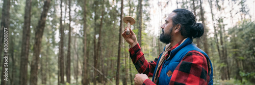 A mushroom picker man with a basket holds a mushroom in his hands in the forest. photo
