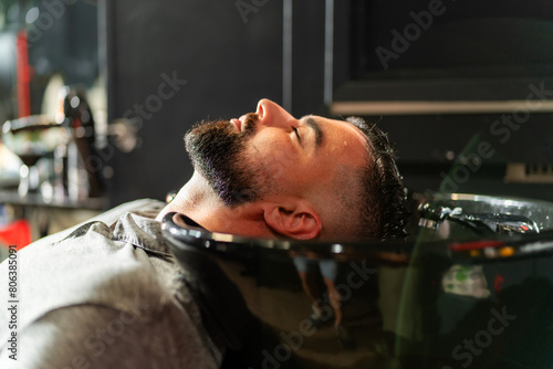 A man relaxes during a professional beard wash at a modern barbershop, highlighting meticulous grooming and personal care practices.