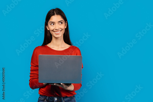 Εκτύπωση καμβά A woman wearing a red shirt is holding a laptop in her hands, displaying a focused expression