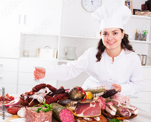 Cook in uniform costs near table with smoked products and sausage and holds in hand plate with jamon photo