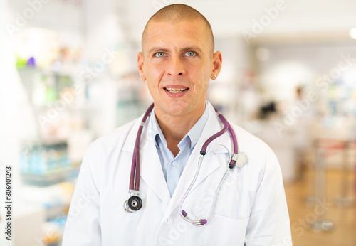Portrait of male pharmacist in white coat standing in chemist shop.