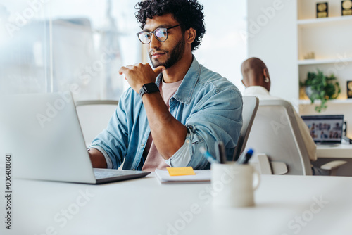 Focused young man working at laptop in bright office