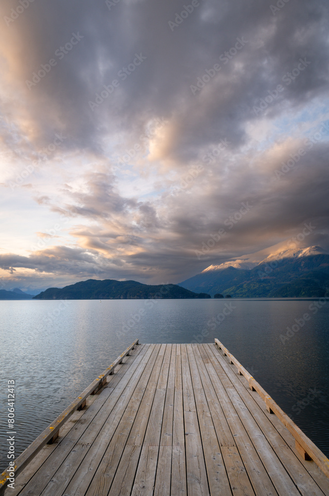 Wooden boat dock leading out to a lake with calm waters with a sunset sky. Harrison Lake, east of the lake are the Lillooet Ranges while to the west are the Douglas Ranges, British Columbia, Canada. Wooden boat dock leading out to a lake with calm waters with a sunset sky. Harrison Lake, east of the lake are the Lillooet Ranges while to the west are the Douglas Ranges, British Columbia, Canada.