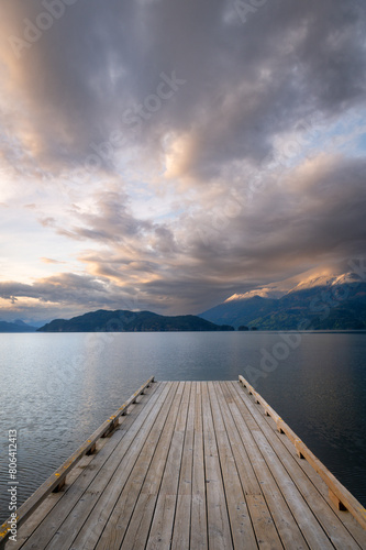 Wooden boat dock leading out to a lake with calm waters with a sunset sky. Harrison Lake  east of the lake are the Lillooet Ranges while to the west are the Douglas Ranges  British Columbia  Canada. 