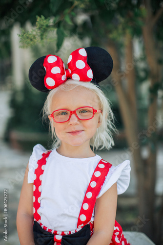 Portrait of a little blond girl with red glasses wearing Minnie Mouse ears