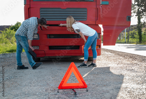 Man and woman truckers, having problem with the truck, warning triangle in front of vehicle