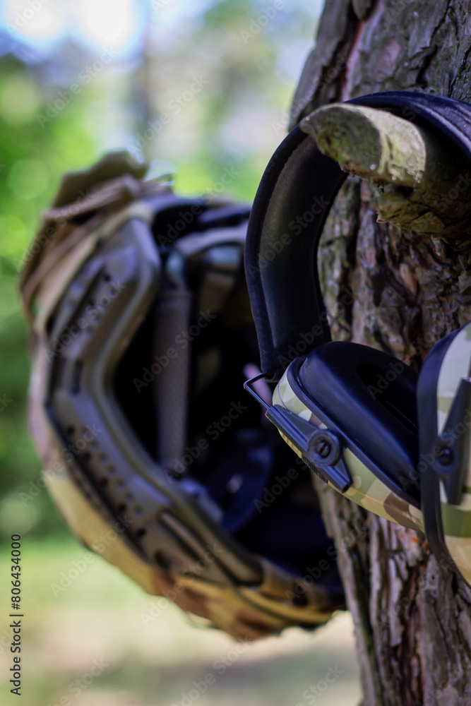 Fototapeta premium A tactical helmet and active tactical headphones hang on a tree branch. Defense of the military, military operations. War in Ukraine