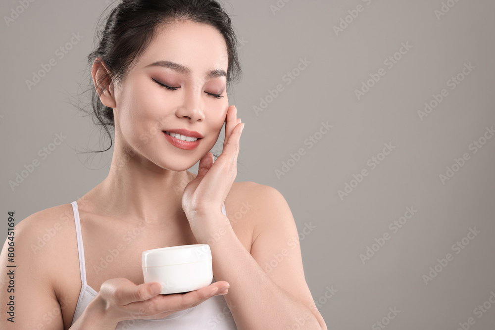 Happy woman applying face cream on grey background, space for text Happy woman applying face cream on grey background, space for text