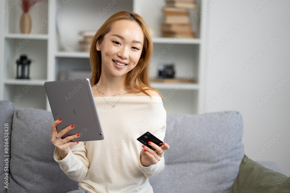 Young Asian Woman With Tablet And Credit Card On Sofa, Smiling At Home, Online Shopping, Modern Technology Usage, Comfortable Living Young Asian Woman With Tablet And Credit Card On Sofa, Smiling At Home, Online Shopping, Modern Technology Usage, Comfortable Living
