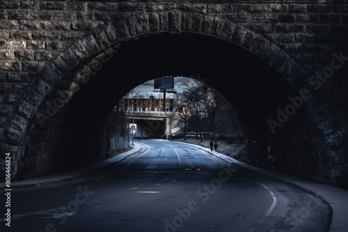 Person walks under dark bridge with tints of monochrome landscape
