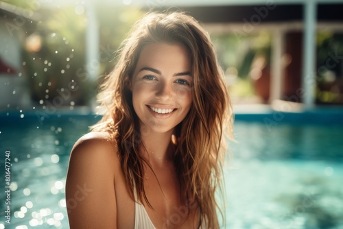 A Radiant Young Woman with Flowing Hair and a Serene Smile Standing Gracefully in Front of a Sparkling Azure Swimming Pool on a Sunny Day