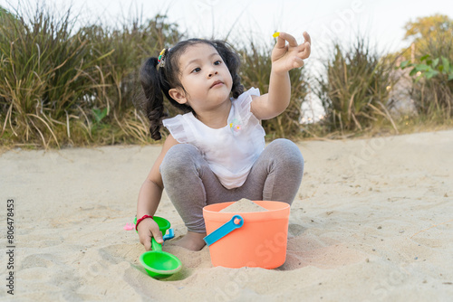 Asian cute little girl is playing sand on the beach very happy.