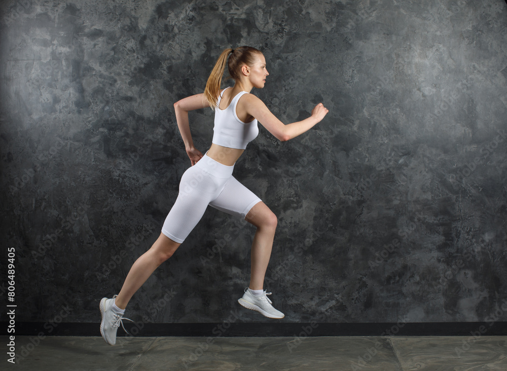 young sportswoman in white sportswear run near black marble wall