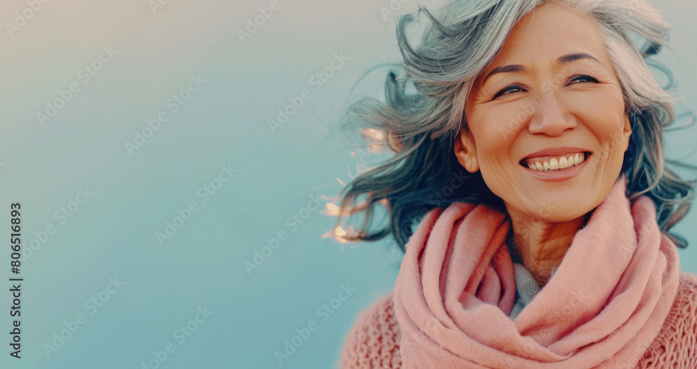 A stylish senior woman with gray hair smiling, wearing a pink scarf, standing against a pastel background. A stylish senior woman with gray hair smiling, wearing a pink scarf, standing against a pastel background.