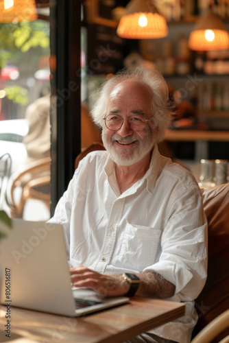 A cheerful senior man using a laptop in a cafe bathed in natural light.