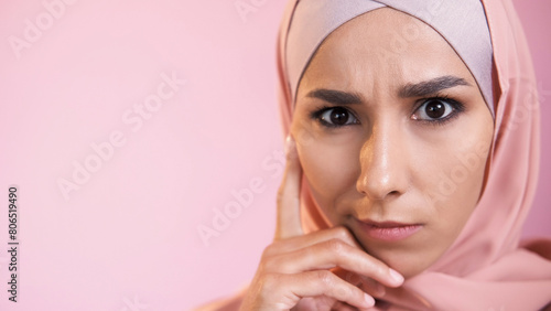 Confused face. Pensive expression. Portrait of concerned serious skeptic woman in hijab thinking isolated on pink empty space background.