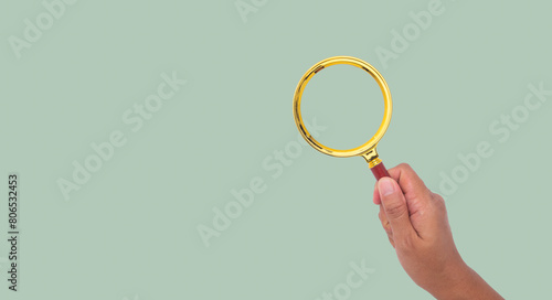 Close-up of a woman's hand holding a magnifying glass against a green background.