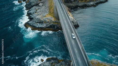 Aerial view of a car driving on a bridge over the ocean, with ocean waves crashing against rocks, taken with drone photography and aerial photography from a road trip in Norway 